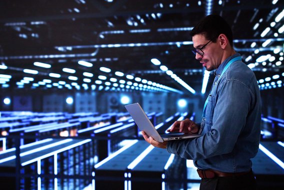 IT-Spezialist arbeitet mit Laptop in einem modernen, blau beleuchteten Serverraum.