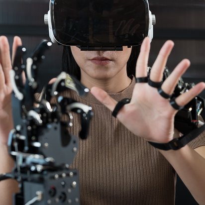 Frau mit KI-Technologie Eine Person mit VR- oder AR-Brille interagiert mit erhobenen Händen mit einer Roboterhand.