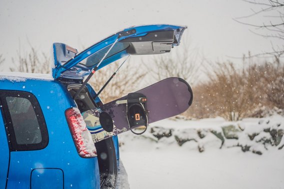 Snowboard im Kofferraum eines blauen Autos bei Schneefall