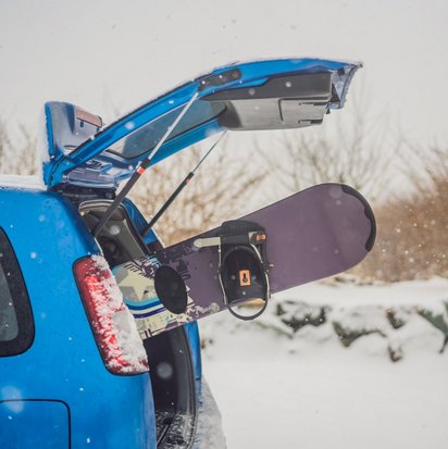 Snowboar steckt im Kofferraum eines blauen Autos im Winter
