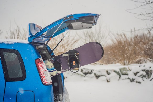 Snowboar steckt im Kofferraum eines blauen Autos im Winter