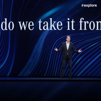 Ein Sprecher in dunklem Anzug steht auf einer Bühne vor einem blauen Hintergrund mit wellenförmigen Mustern, während über ihm der Text "So, where do we take it from here?" projiziert wird.WiederholenClaude kann Fehler machen. Bitte überprüfen Sie die Antworten.