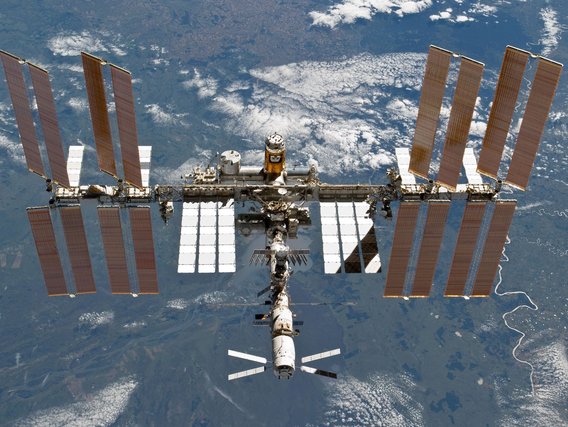 Die Internationale Raumstation ISS mit ausgebreiteten Solarpaneelen schwebt über der blauen Erde.
