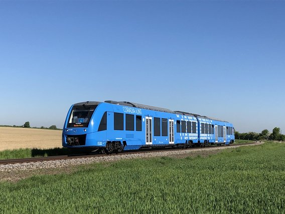 Blauer Wasserstoffzug "Coradia iLint" fährt durch grüne Landschaft mit Feldern bei strahlend blauem Himmel.