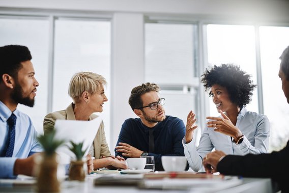 Fünf Personen sitzen zusammen an einem Tisch und sind in eine Diskussion vertieft.