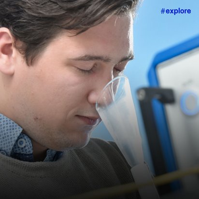 Nahaufnahme eines jungen Mannes, der durch einen transparenten Schlauch an einem wissenschaftlichen Messgerät riecht oder die Luftqualität prüft. Im Hintergrund ist das blau-silberne Kontrollpanel des Geräts zu sehen.