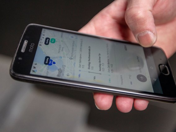 Smartphone mit geöffneter MOIA-App zeigt eine Kartenansicht mit Routenplanung und Haltestellen.