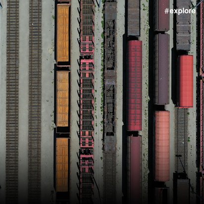 Luftaufnahme eines großen Güterbahnhofs mit parallelen Gleisen und bunten Güterwaggons in verschiedenen Farben (rot, orange, braun).