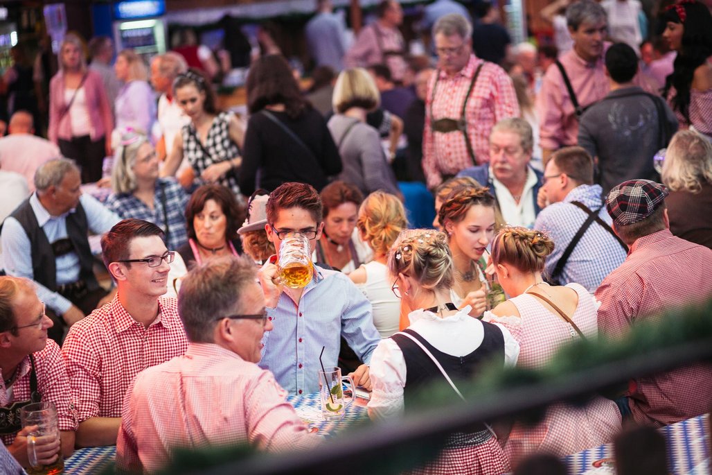 Blick auf eine überfüllte Festveranstaltung mit Personen in traditioneller Kleidung, viele in karierter Tracht, die an Biertischen sitzen und gesellig feiern.