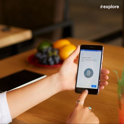 Eine Person mit Türkis-Ohrring nutzt die Fingerabdruck-Authentifizierung auf ihrem Smartphone, während ein Getränk und Obst auf einem Holztisch stehen.