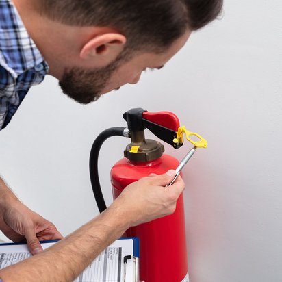 Mann kontrolliert einen Feuerlöscher und notiert die Ergebnisse auf einem Klemmbrett