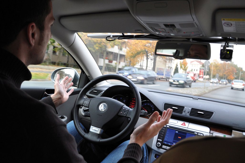 Im Innenraum eines Volkswagens demonstriert ein Fahrer freihändiges Fahren während der Fahrt durch die Stadt. Die Szene zeigt die praktische Anwendung autonomer Fahrassistenzsysteme.