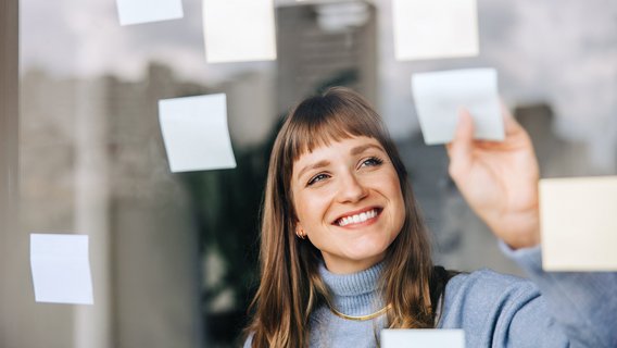 Eine junge Frau klebt Post-its an eine Scheibe