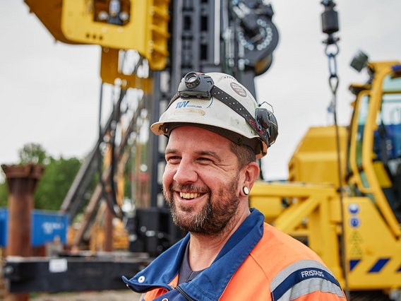 Lächelnder TÜV NORD-Mitarbeiter mit Schutzhelm und Warnkleidung auf einer Baustelle.