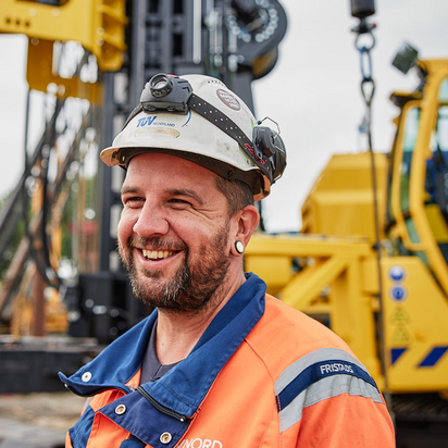 TÜV NORD-Krane Lächelnder TÜV NORD-Mitarbeiter mit Schutzhelm und Warnkleidung auf einer Baustelle.