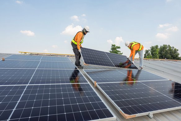 Zwei Arbeiter montieren Solarpanels auf einem Dach bei sonnigem Wetter.