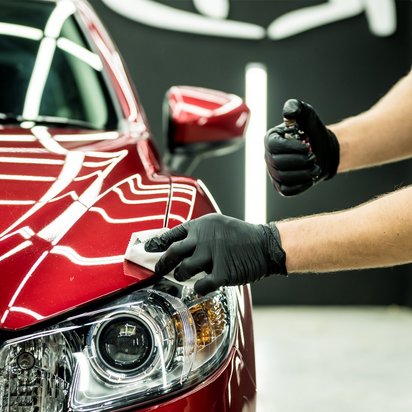 Professionelle Fahrzeugpflege: Glanz und Schutz für Ihr Auto Ein rotes Auto wird von einer Person mit schwarzen Handschuhen sorgfältig poliert. Die glänzende Oberfläche des Fahrzeugs reflektiert das Licht, während die Person ein Pflegemittel aufträgt, um den Lack zu schützen und zu verschönern.