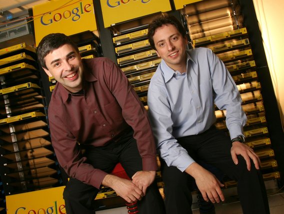 Larry Page (l.) und Sergey Brin (r.) lächeln vor Google-Serverracks mit gelben Gehäusen in einem Rechenzentrum.