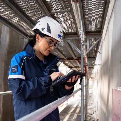 TÜV NORD-Mitarbeiterin mit Helm prüft bauliche Details auf einer Baustelle und dokumentiert mögliche Baumängel.