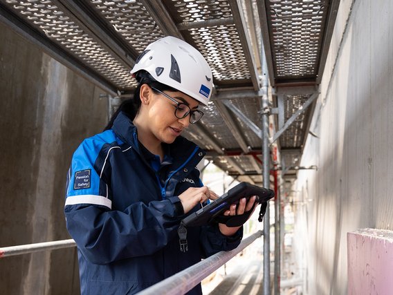 TÜV NORD-Mitarbeiterin mit Helm prüft bauliche Details auf einer Baustelle und dokumentiert mögliche Baumängel.