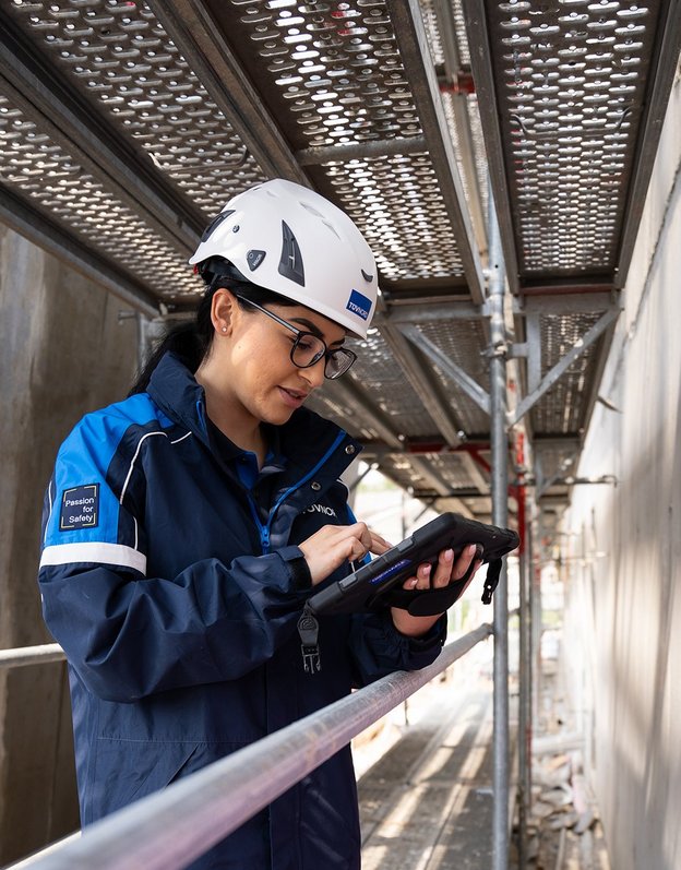 TÜV NORD-Mitarbeiterin mit Helm prüft bauliche Details auf einer Baustelle und dokumentiert mögliche Baumängel.