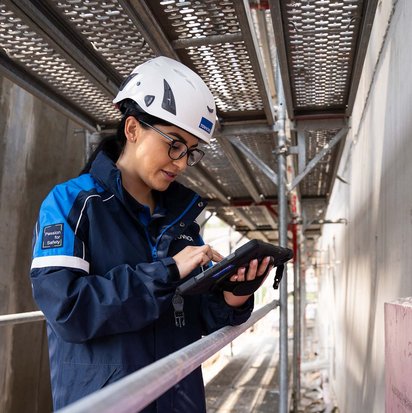 TÜV NORD-Mitarbeiterin mit Helm prüft bauliche Details auf einer Baustelle und dokumentiert mögliche Baumängel.