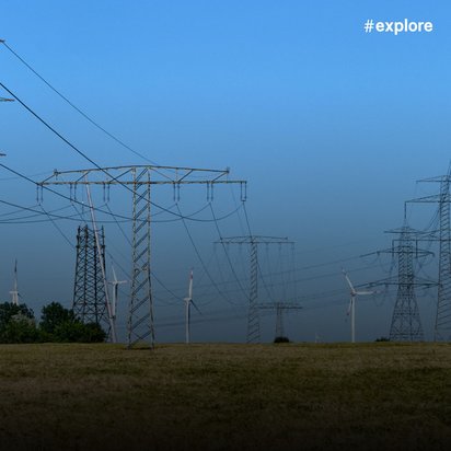 Stromnetz: Hochspannungsmasten und Stromkabel erstrecken sich über eine weite Wiese. Windturbinen sind im Hintergrund zu sehen.