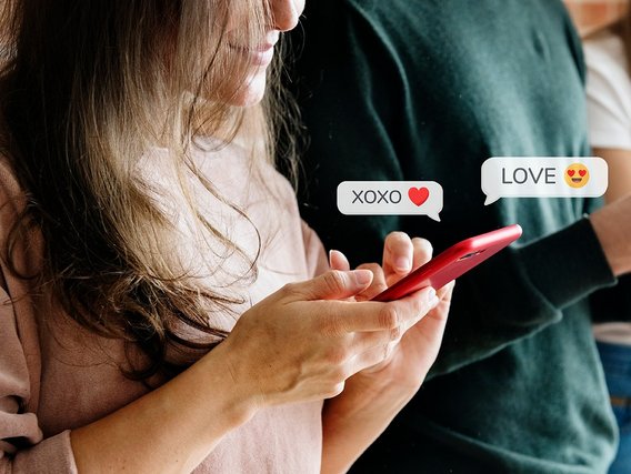 Eine Person mit langen Haaren tippt auf einem roten Smartphone mit darüber schwebenden Chat-Blasen, die "XOXO ❤️" und "LOVE 😍" anzeigen.