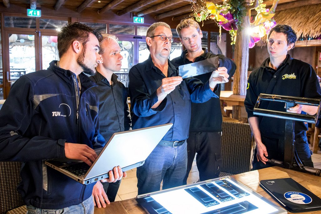 Fünf Personen stehen in einem Raum eines Freizeitparks. Eine Person mit dem TÜV NORD-Logo auf der Jacke hält einen Laptop, während eine andere Person ein Röntgenbild in den Händen hält. Auf dem Tisch vor ihnen liegen mehrere Röntgenbilder. 