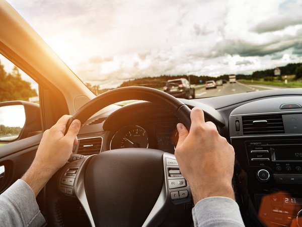 Hände am Lenkrad eines Autos, die Sonne scheint.