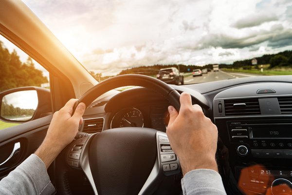 Hände am Lenkrad eines Autos, die Sonne scheint.