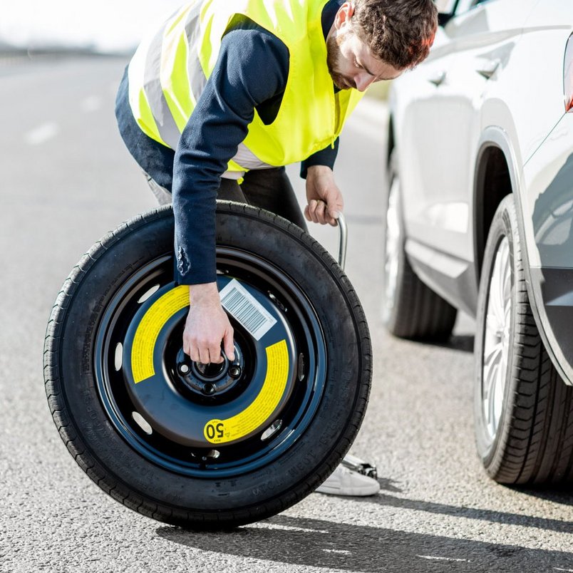 Person wechselt Ersatzrad auf einer Autobahn