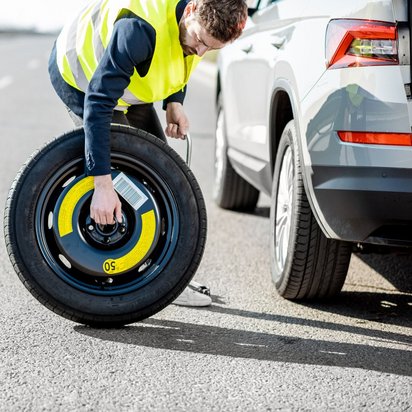 Person wechselt Ersatzrad auf einer Autobahn
