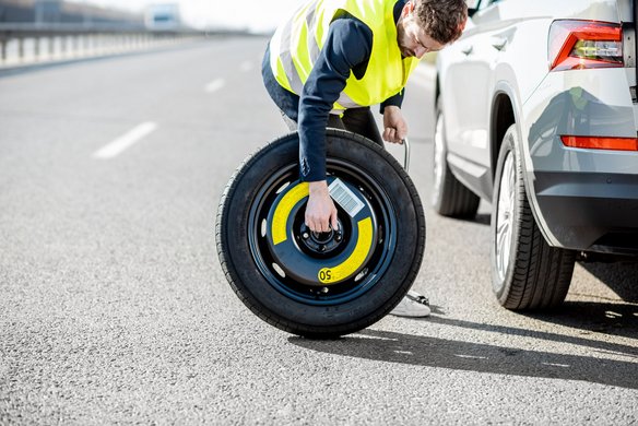 Person wechselt Ersatzrad auf einer Autobahn