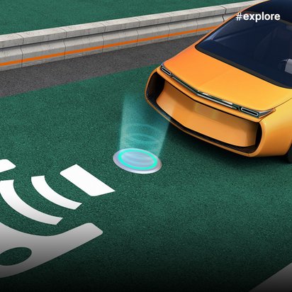 Ein oranges Elektroauto mit schwarzem Glasdach steht auf einer grünen Fahrspur mit weißen Symbolen für drahtlose Energieübertragung, während türkise Lichtkreise die aktive Induktionsladung während der Fahrt visualisieren. Die futuristische Darstellung zeigt kontaktloses kabelloses Laden von Elektrofahrzeugen direkt auf der Straße.