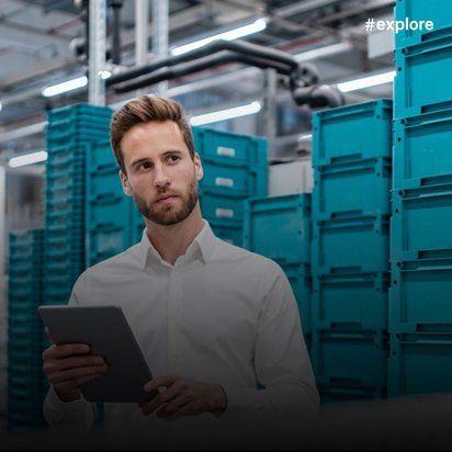 Junger Mann in weißem Hemd mit Tablet in einem modernen Logistikzentrum; gestapelte türkisfarbene Transportboxen im Hintergrund.