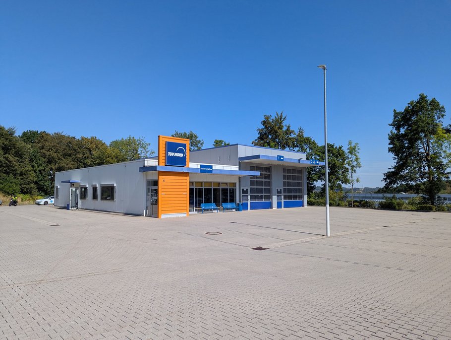 Außenansicht einer TÜV NORD Station mit orange-blauem Eingangsbereich und großem, leerem Parkplatz.