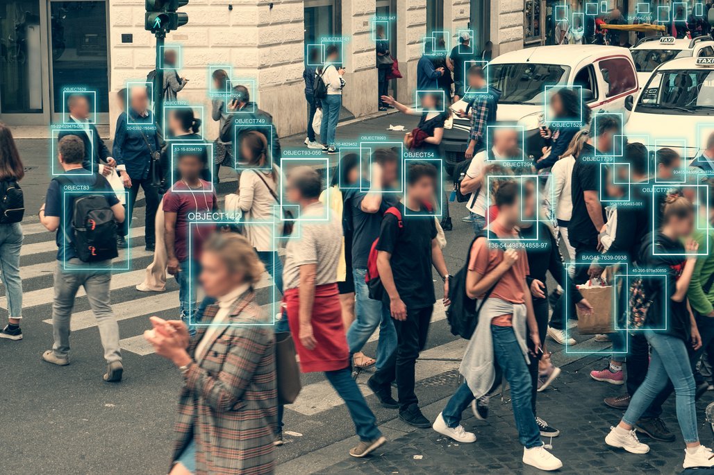 Straßenszene mit Fußgängern an Zebrastreifen, überlagert mit digitalen Erkennungsrahmen und Objekt-IDs. Demonstration von KI-basierter Personenerkennung und Überwachungstechnologie im urbanen Raum.