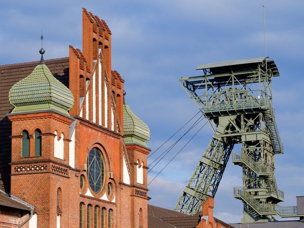 Backsteingebäude mit Zwiebeltürmen und Förderturm einer alten Zeche bei blauem Himmel