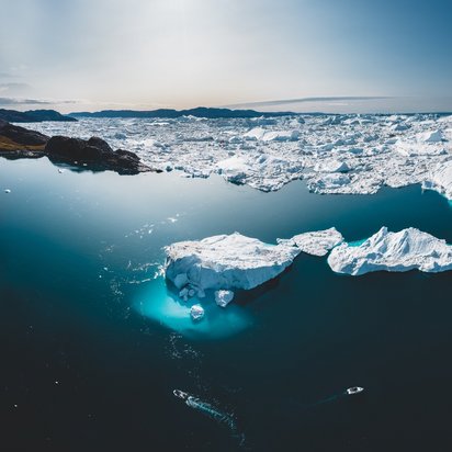 Luftaufnahme von schmelzenden Eisbergen in der Arktis mit zwei Booten im Wasser