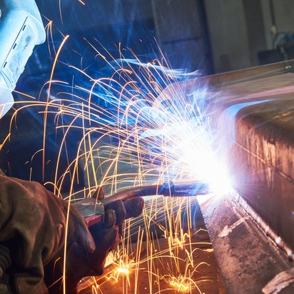Nahaufnahme eines Lichtbogenschweißvorgangs mit sprühenden Funken an einem großen Metallbauteil.