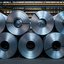 Mehrere aufgerollte Stahlbleche lagern in einer Fabrikhalle, bereit für die Weiterverarbeitung in der Metallindustrie