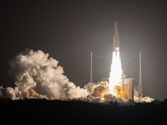 Rakete startet bei Nacht mit orange-weißen Flammen und großen Rauchwolken von einer Startrampe.