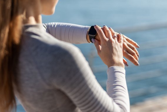 Frau prüft ihre Smartwatch im Freien mit Blick auf das Wasser im Hintergrund.
