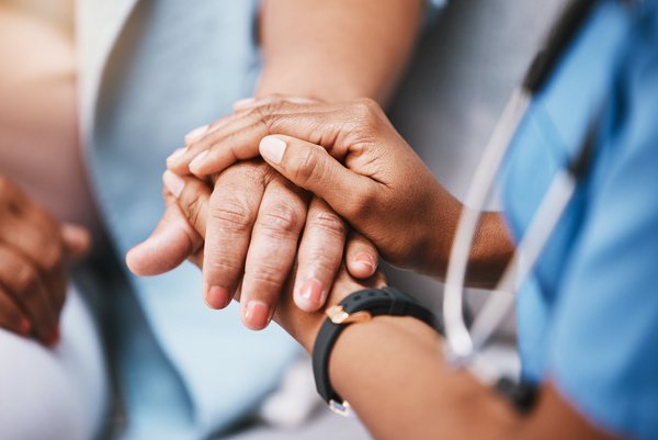 Pflegekraft hält tröstend die Hände einer älteren Person in einer einfühlsamen Geste.