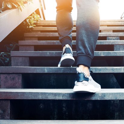  Person in sportlichen Schuhen steigt eine Holztreppe hinauf, symbolisiert den Weg zum Erfolg im Coaching KickOFF Programm des TÜV NORD technischen Schulungszentrums.