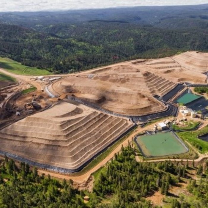 Luftaufnahme einer großen Tagebau-Mine, umgeben von üppigen grünen Wäldern und Hügeln. Die Mine zeigt terrassenförmige Abbauflächen und mehrere Wasserbecken, die für die Verarbeitung und Umweltmanagement genutzt werden.
