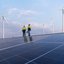 Zwei TÜV NORD-Ingenieure prüfen Solarmodule vor Windrädern unter blauem Himmel
