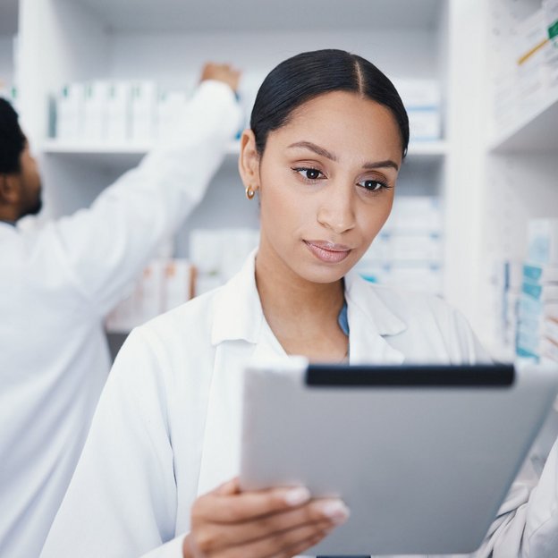 Apothekerin prüft Informationen auf einem Tablet in einer modern eingerichteten Apotheke.