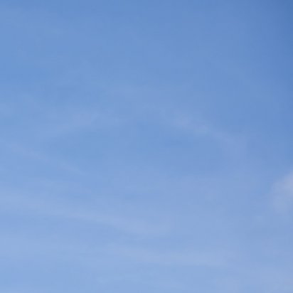 Ein Drohne fliegt vor blauem Himmel neben einem weißen Windkraftanlagen-Turm mit rotem Kran im Hintergrund. Die Drohne führt vermutlich eine Inspektion der Windkraftanlage durch.